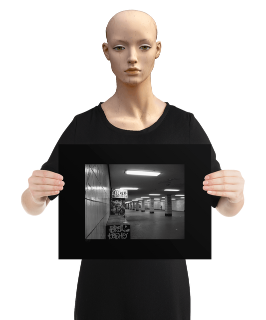 un4rt - a black and white photographie of a former underground trespas that once was part of the train station "alexanderplatz in berlin. tiled square columns support the ceiling. the left wall also has a porch of an old flower shop. the porch is full of graffities and the sign of the shop advertises "blumen". the image is held by a mannequin.