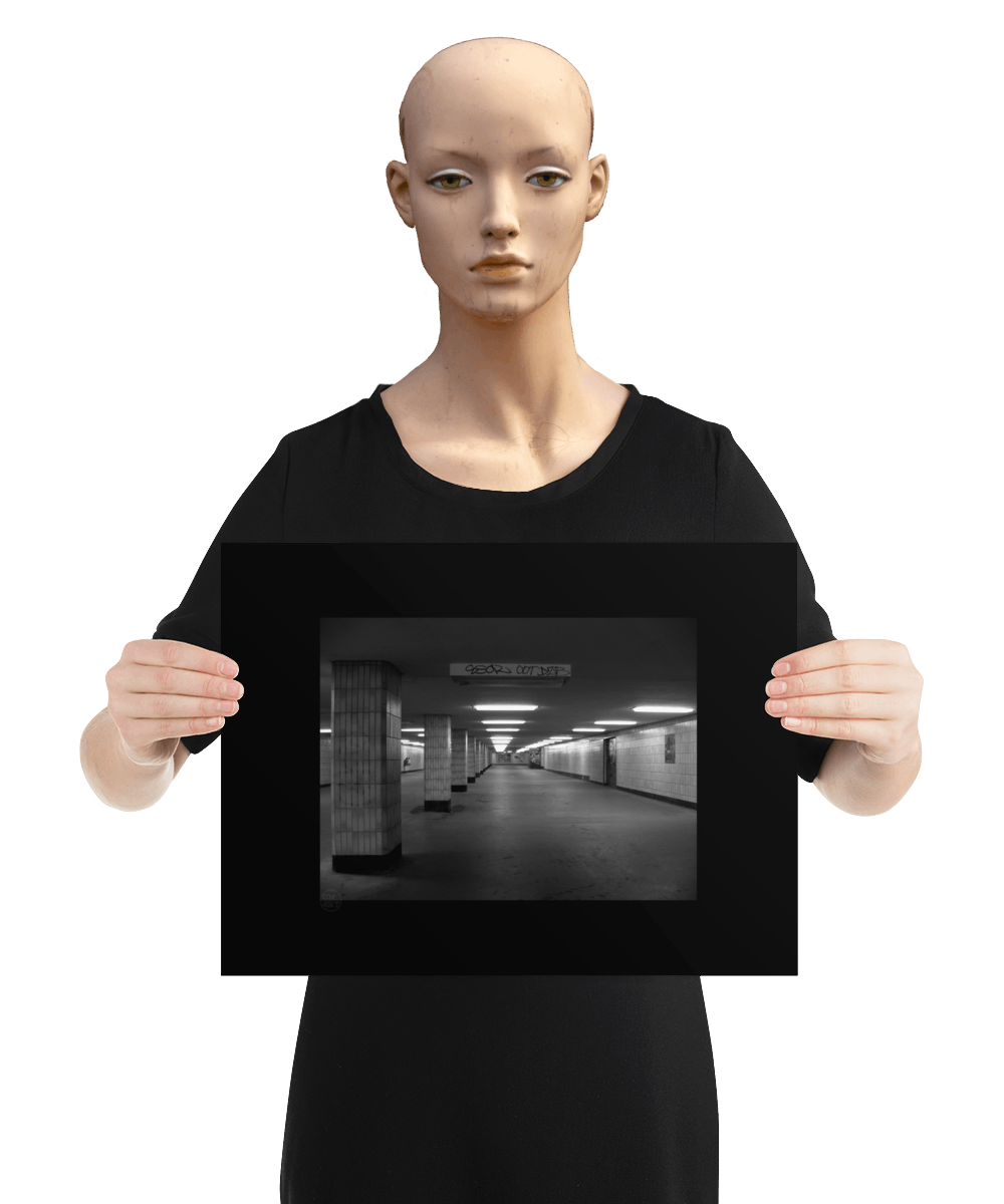 un4rt - a black and white photographie of a former underground trespas that once was part of the train station "alexanderplatz in berlin. tiled square columns support the ceiling. a closed door on the right side. one light on the ceiling does´t work. the image is held by a mannequin.