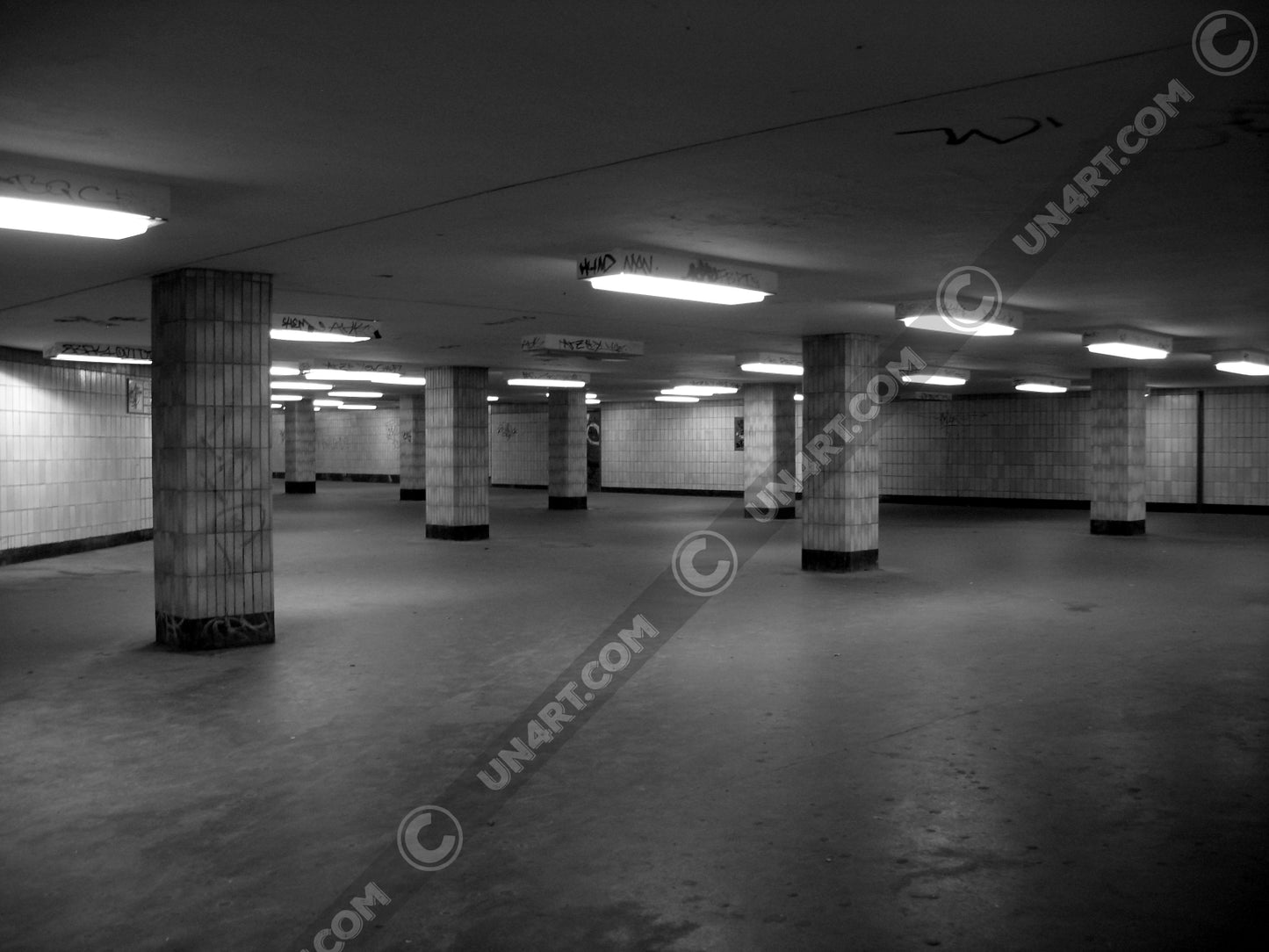 un4rt - a black and white photographie of a former underground trespas that once was part of the train station "alexanderplatz in berlin. tiled square columns support the ceiling. graffities on the columns and the ceiling.