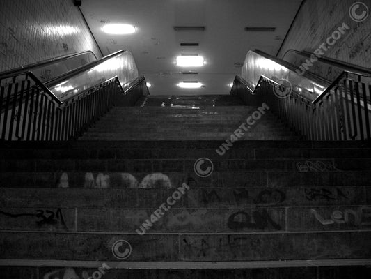un4rt - a black and white photographie of a former underground trespas that once was part of the train station "alexanderplatz" in berlin. stairway. graffities on the stairs and the walls.