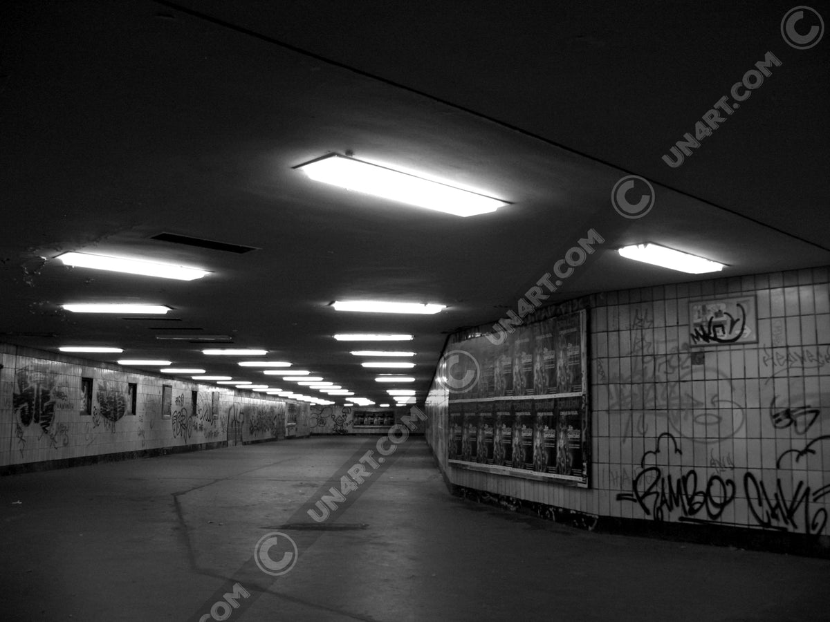 un4rt - a black and white photographie of a former underground trespas that once was part of the train station "alexanderplatz" in berlin. advertisings and graffities on the wall.