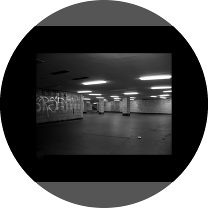 un4rt - a black and white photographie of a former underground trespas that once was part of the train station "alexanderplatz" in berlin. graffities on the wall, trash on the ground. some lights on the ceiling don´t work. a stairway at the end of the trespas.