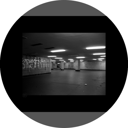 un4rt - a black and white photographie of a former underground trespas that once was part of the train station "alexanderplatz" in berlin. graffities on the wall, trash on the ground. some lights on the ceiling don´t work. a stairway at the end of the trespas.