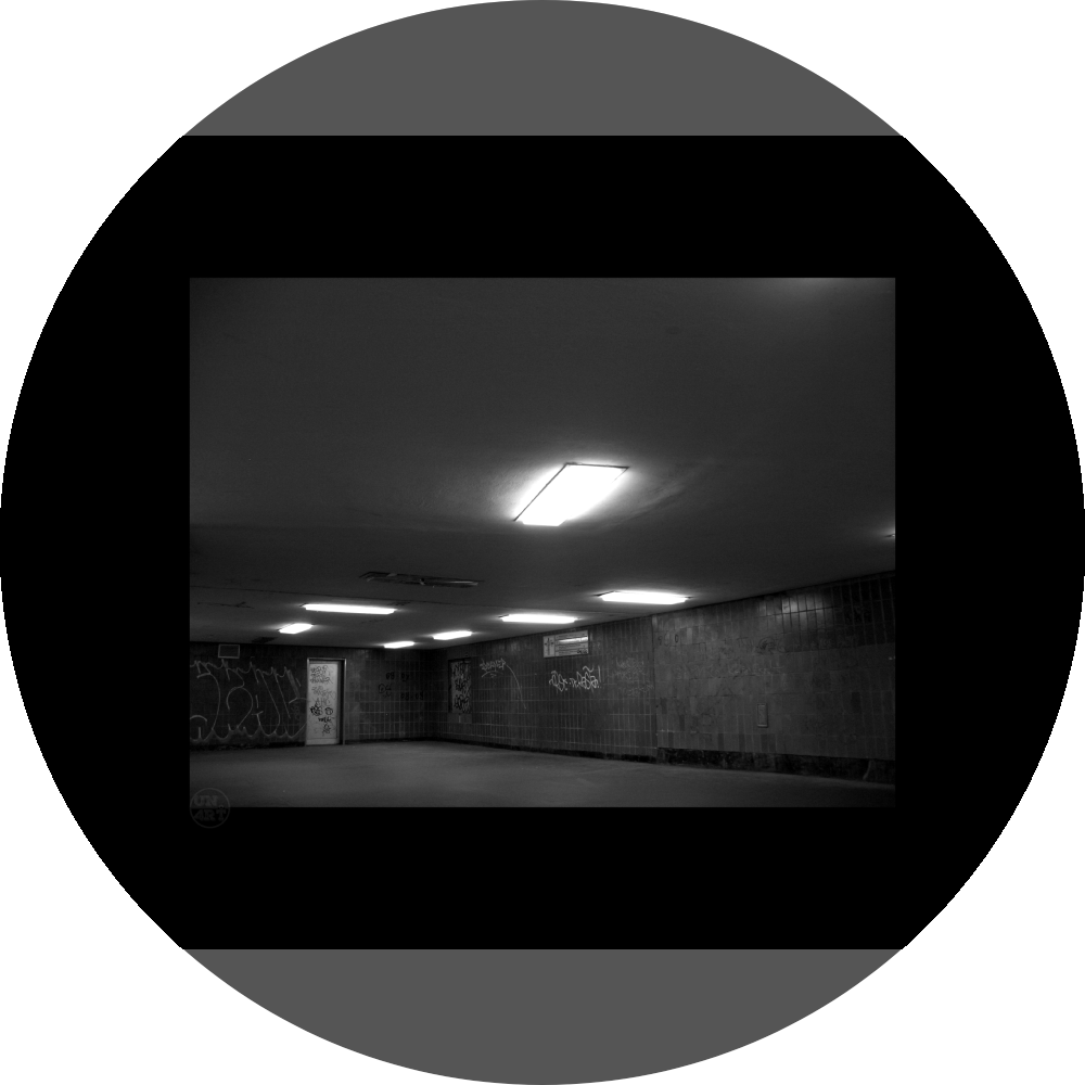 un4rt - a black and white photographie of a former underground trespas that once was part of the train station "alexanderplatz" in berlin. the image shows a corner with a closed door. graffities on the wall. one lamp on the ceiling is broken.
