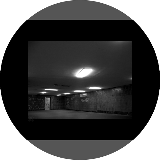 un4rt - a black and white photographie of a former underground trespas that once was part of the train station "alexanderplatz" in berlin. the image shows a corner with a closed door. graffities on the wall. one lamp on the ceiling is broken.