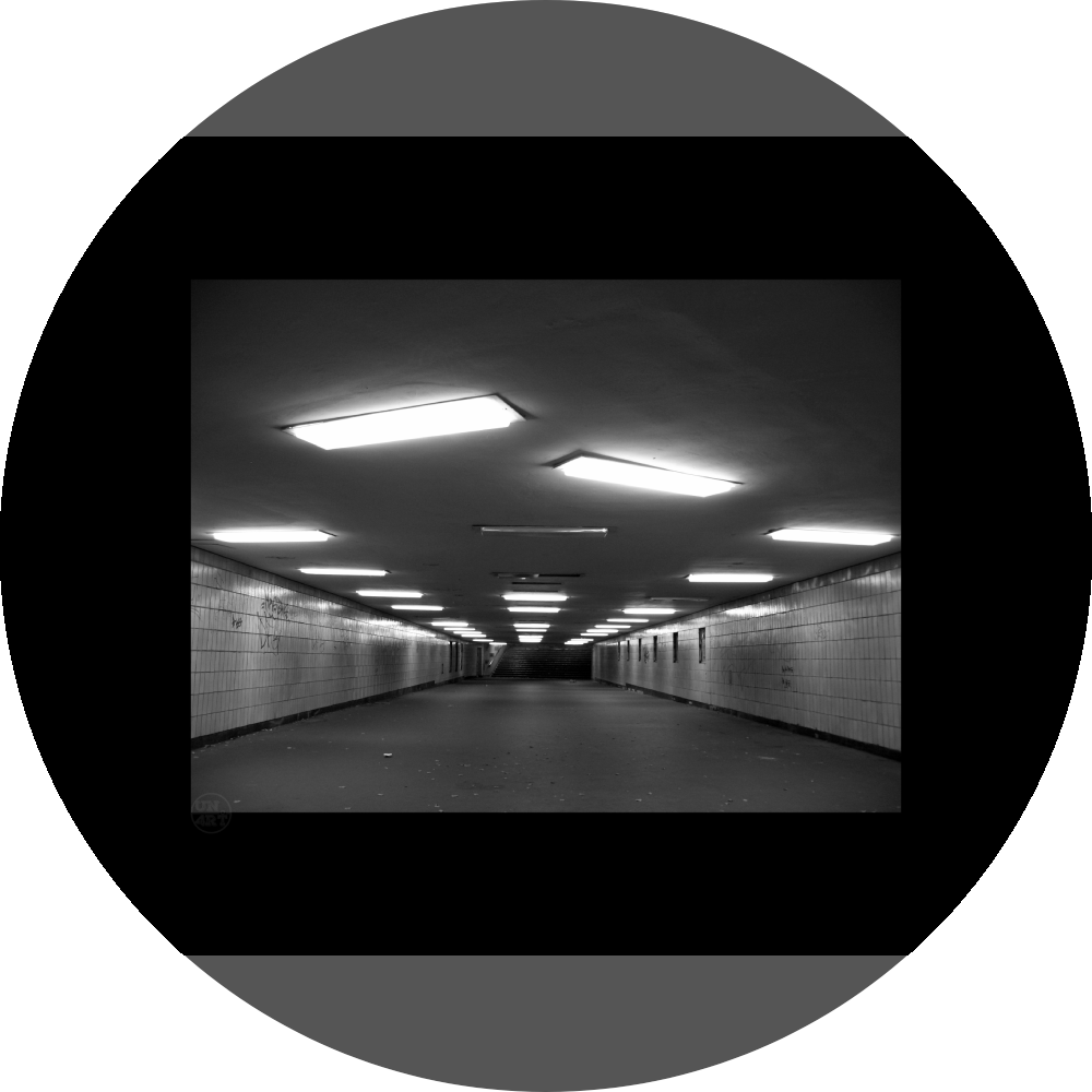 un4rt - a black and white photographie of a former underground trespas that once was part of the train station "alexanderplatz" in berlin. the walls are tiled. some graffities on the walls and placeholders for advertising posters. trash on the floor. some lights n the ceiling don´t work.