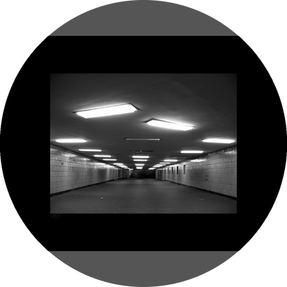 un4rt - a black and white photographie of a former underground trespas that once was part of the train station "alexanderplatz" in berlin. the walls are tiled. some graffities on the walls and placeholders for advertising posters. trash on the floor. some lights n the ceiling don´t work.