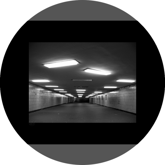 un4rt - a black and white photographie of a former underground trespas that once was part of the train station "alexanderplatz" in berlin. the walls are tiled. some graffities on the walls and placeholders for advertising posters. trash on the floor. some lights n the ceiling don´t work.