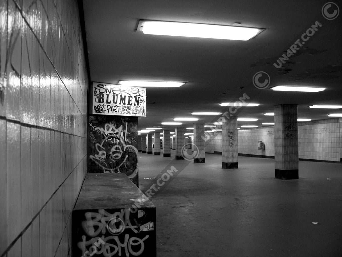 un4rt - a black and white photographie of a former underground trespas that once was part of the train station "alexanderplatz" in berlin. tiled square columns support the ceiling. the left wall also has a porch of an old flower shop. the porch is full of graffities and the sign of the shop advertises "blumen".