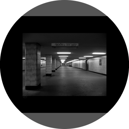 un4rt - a black and white photographie of a former underground trespas that once was part of the train station "alexanderplatz" in berlin. tiled square columns support the ceiling. a closed door on the right side. one light on the ceiling does´t work.