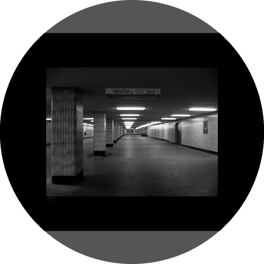 un4rt - a black and white photographie of a former underground trespas that once was part of the train station "alexanderplatz" in berlin. tiled square columns support the ceiling. a closed door on the right side. one light on the ceiling does´t work.