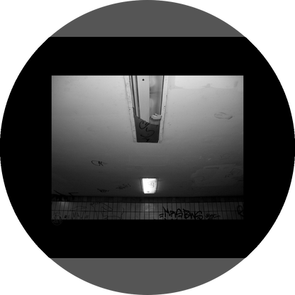 un4rt - a black and white photographie of a former underground trespas that once was part of the train station "alexanderplatz" in berlin. the wall is tiled and coverd with graffities. one of the two lights on the ceiling don´t work anymore. the glas is broken and a newspaper is stuffed into the lamp.