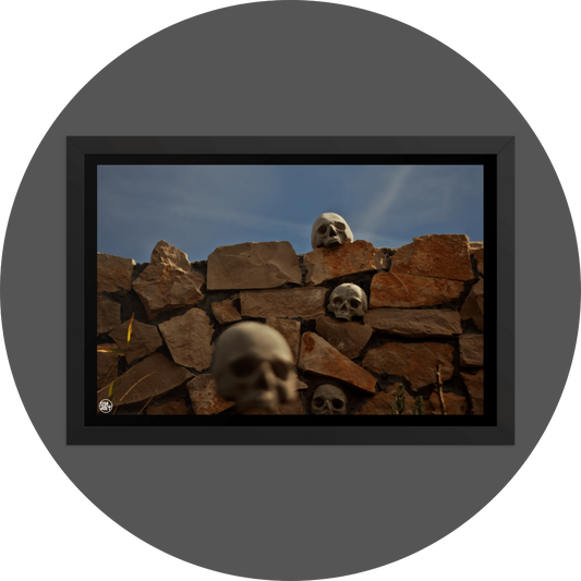 un4rt - the photographie shows a chaotic decorative stone wall with skulls in and on top of it. chemtrails in the sky starting to cover the natural blue of the sky.. one blurry skull in the foregrund.