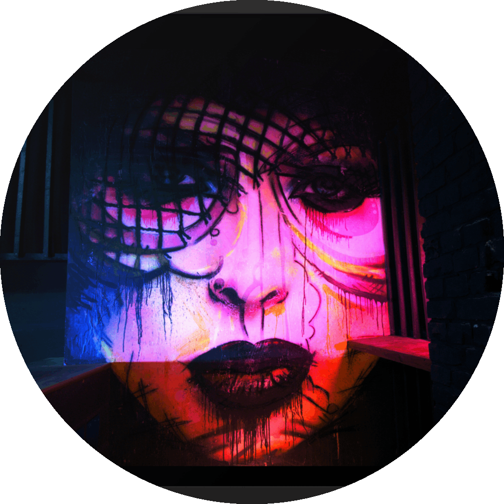 un4rt - the photographie shows a mural of a female face in various colors, pink, yellow, blue, orange. the face is surrounded by black walls, some made of bricks, some made of wood. 