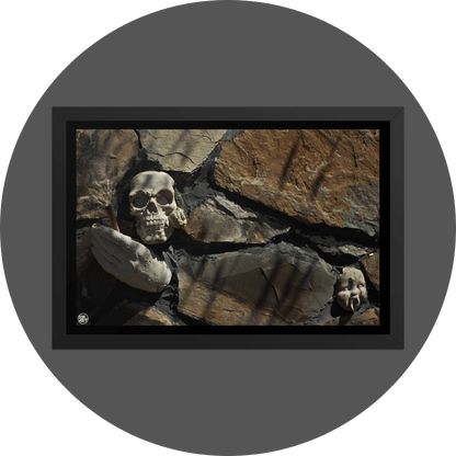 un4rt - the photographie shows some stones that are art of a bigger stone wall. a plaster skull with a rose in its mouth, a plaster hand with a joint and a baby face with plaster vampire teeth decorate the wall.