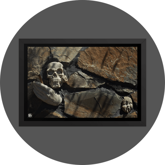 un4rt - the photographie shows some stones that are art of a bigger stone wall. a plaster skull with a rose in its mouth, a plaster hand with a joint and a baby face with plaster vampire teeth decorate the wall.