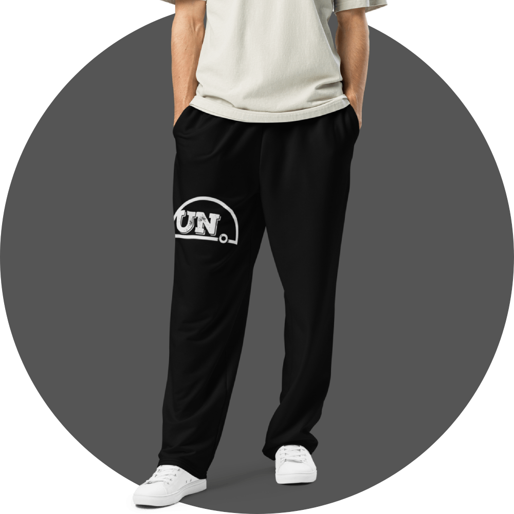 UN4RT black jogger pants, distressed white "UN." semicircle logo on right thigh, straight fit, front view, grey circular background.