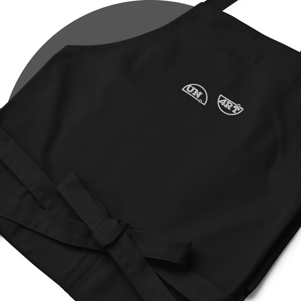 un4rt - the images shows details of a black apron with white embroidery of a splitted "UN4RT"-logo. 