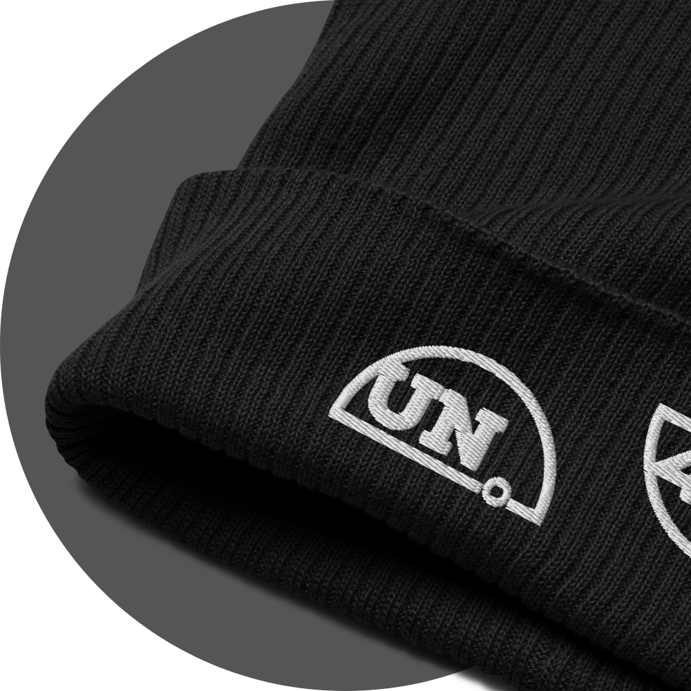 un4rt - the images shows a closeup of a black certified organic cotton beanie with parts of a white embroidery of the splitted "UN4RT-logo.
